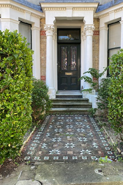 Exterior view of a residential building entrance featuring a curved set of concrete steps leading up to an arched doorway with a white painted trim. The brick facade includes large bay windows with wh